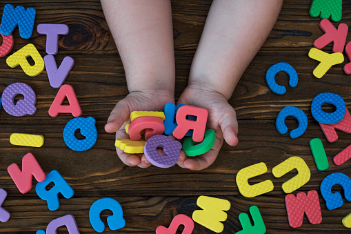 letters of the English alphabet in his hands on a wooden background. education. game.